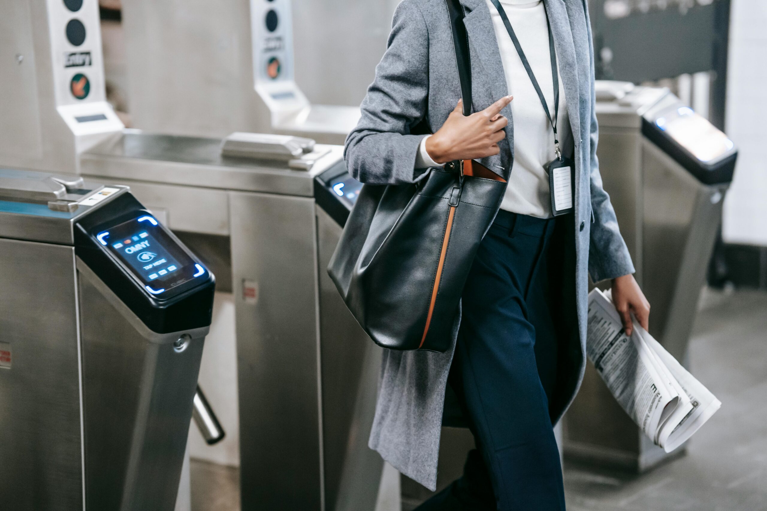 Crop anonymous African American female in formal clothes with newspaper passing through turnstile gates in modern underground station